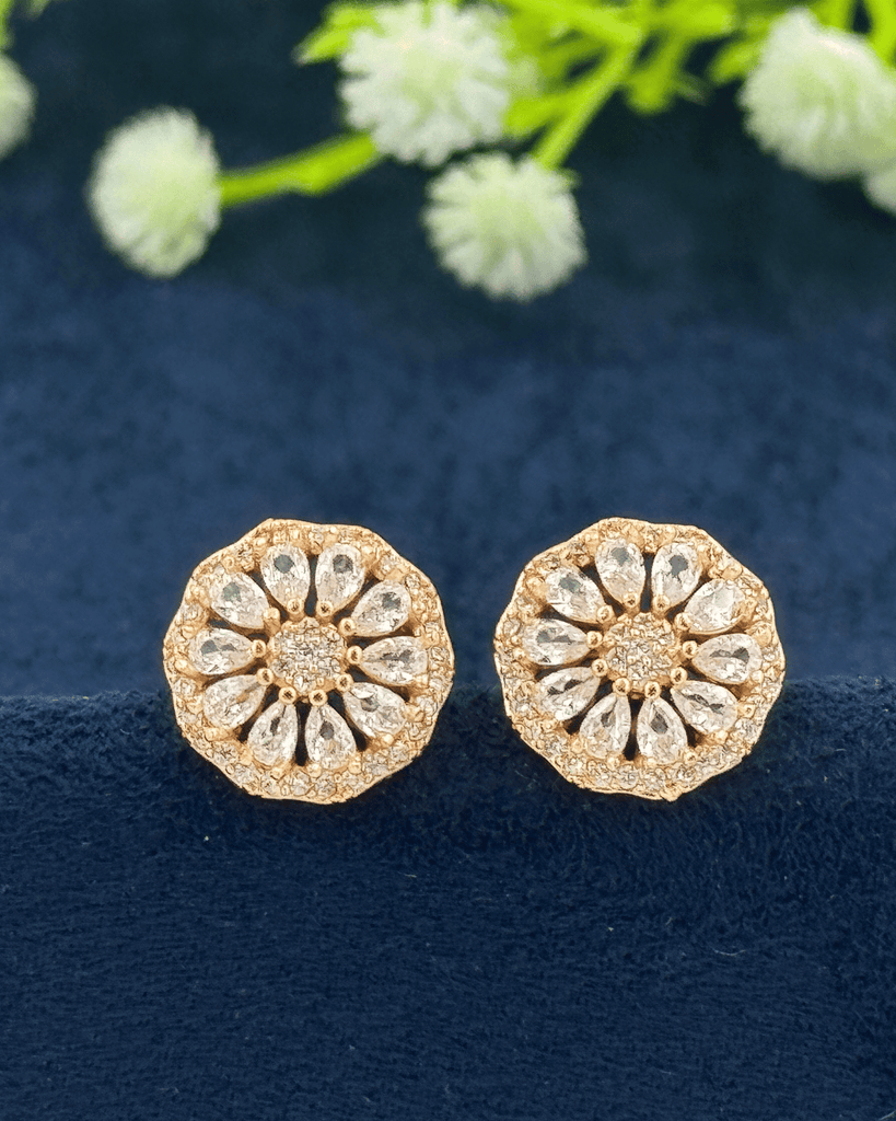 Gold floral earrings with clear stones on a dark blue fabric background