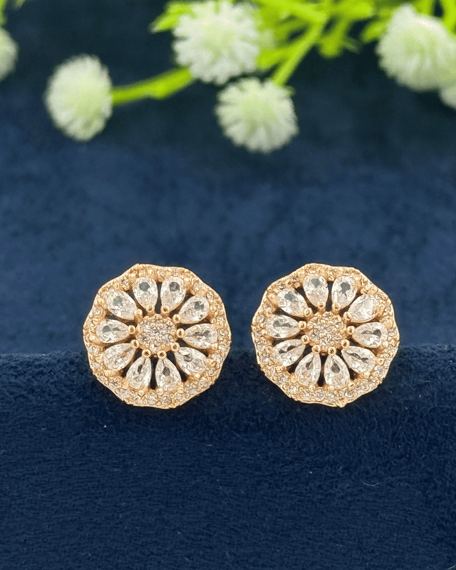 Gold floral earrings with clear stones on a dark blue fabric background